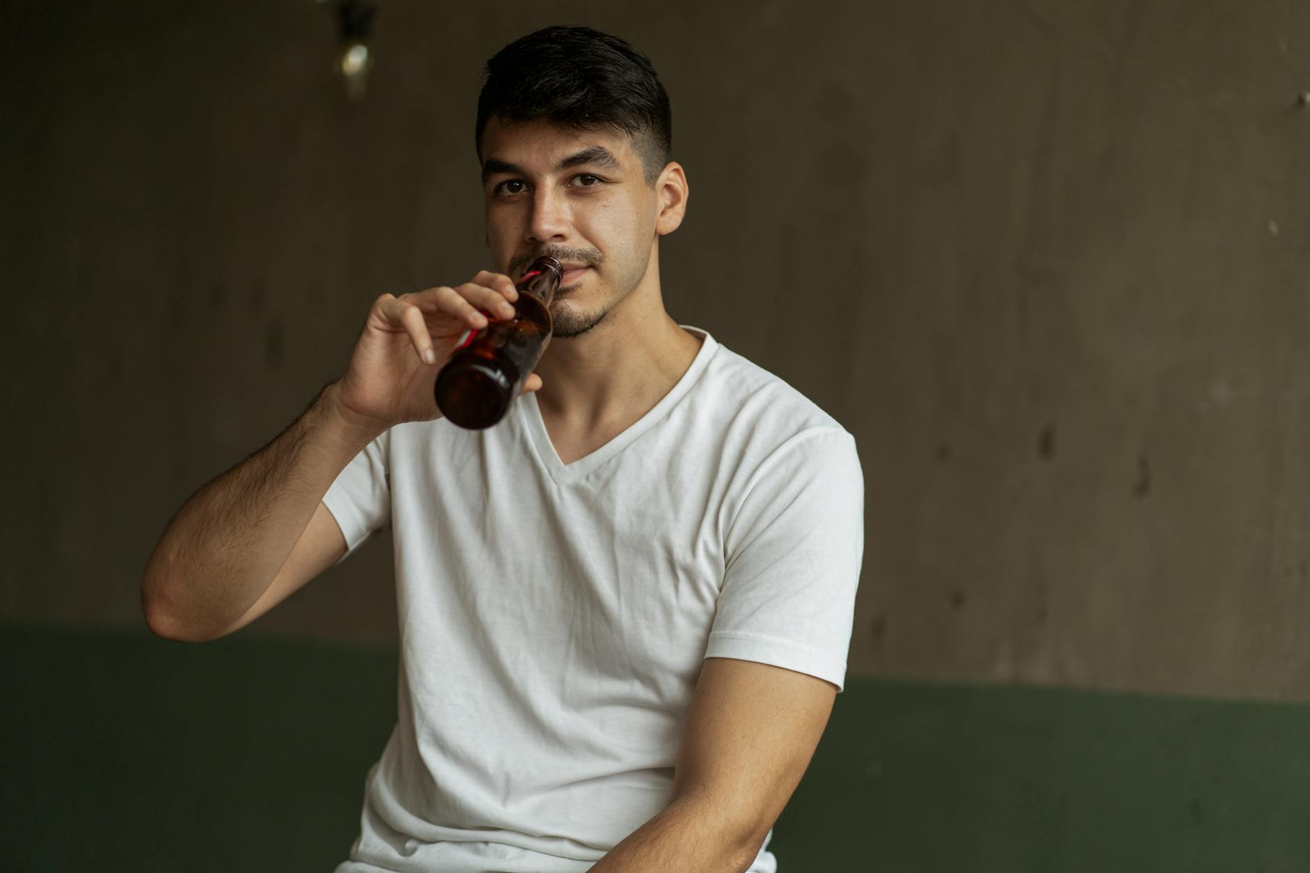 Mężczyzna w domu pije piwo z butelki przy stole