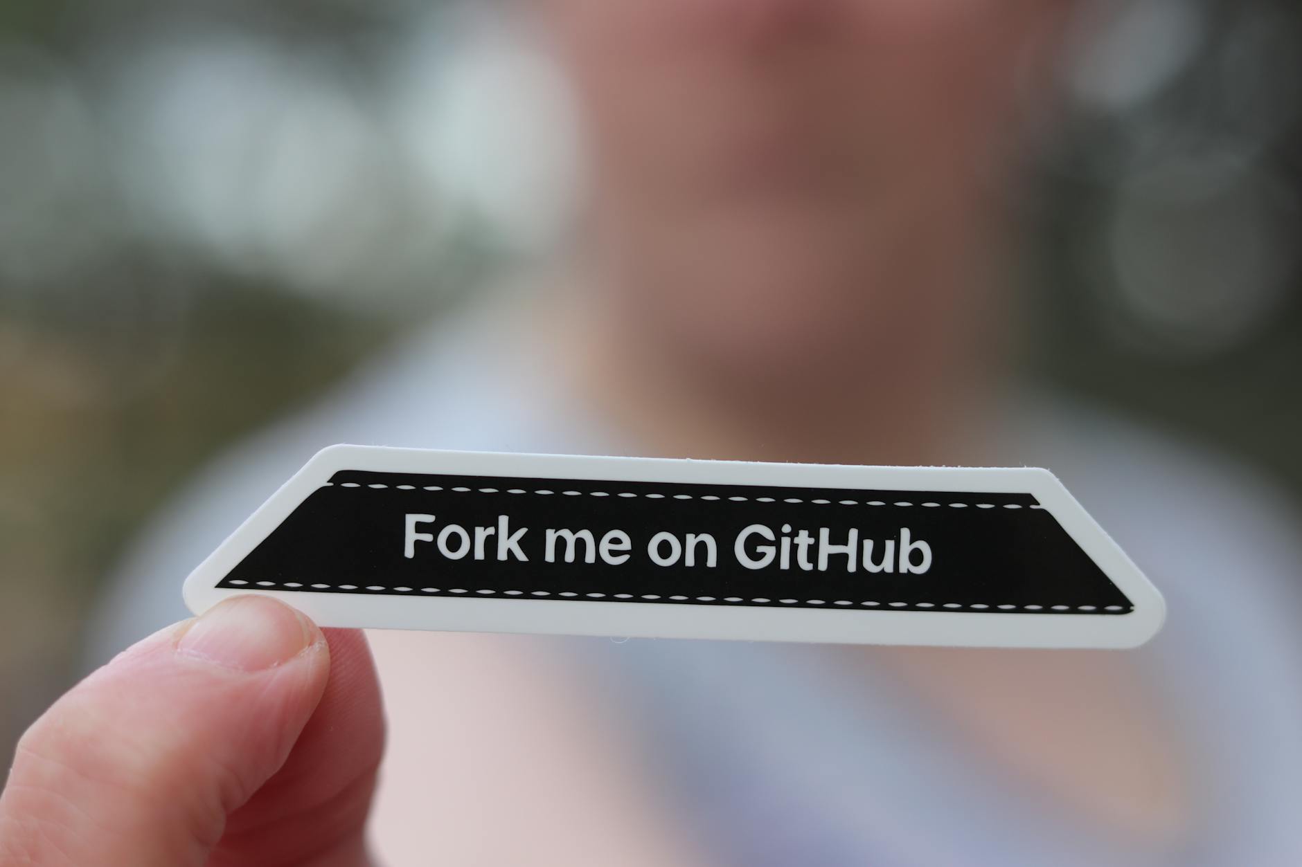 Dłoń trzymająca naklejkę Fork me on GitHub na rozmytym tle Dłoń trzymająca naklejkę Fork me on GitHub na rozmytym tle