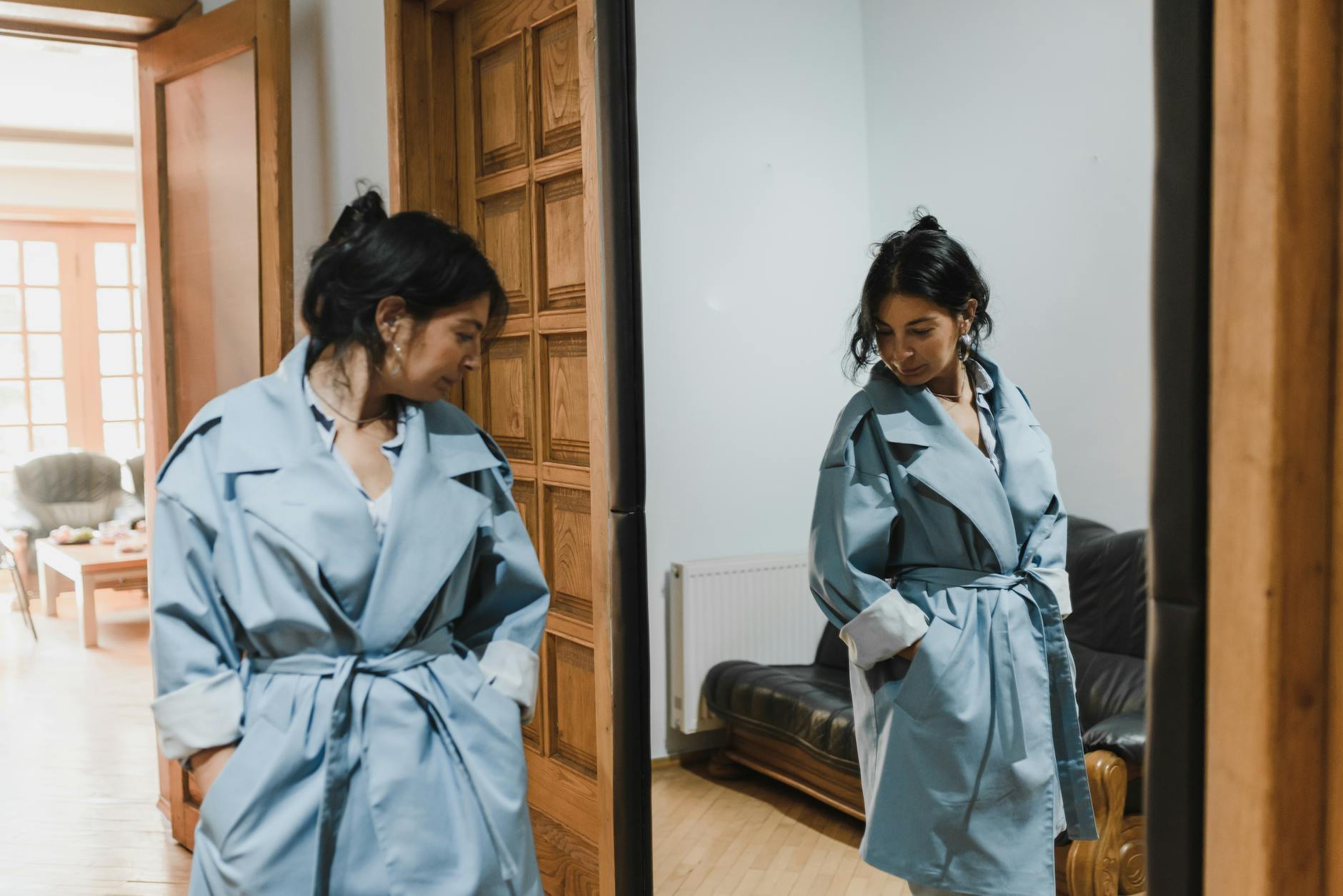 Kobieta w niebieskim trenczu przymierza płaszcz przed lustrem