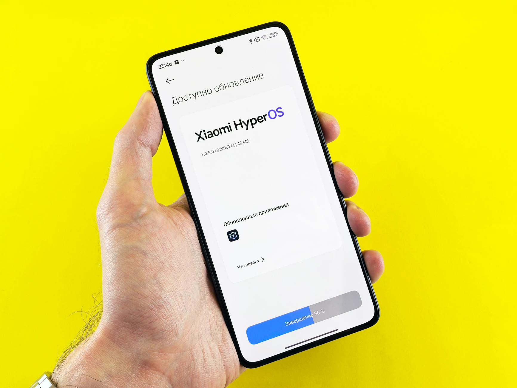 Smartfon z ekranem aktualizacji Xiaomi HyperOS trzymany w dłoni na żółtym tle