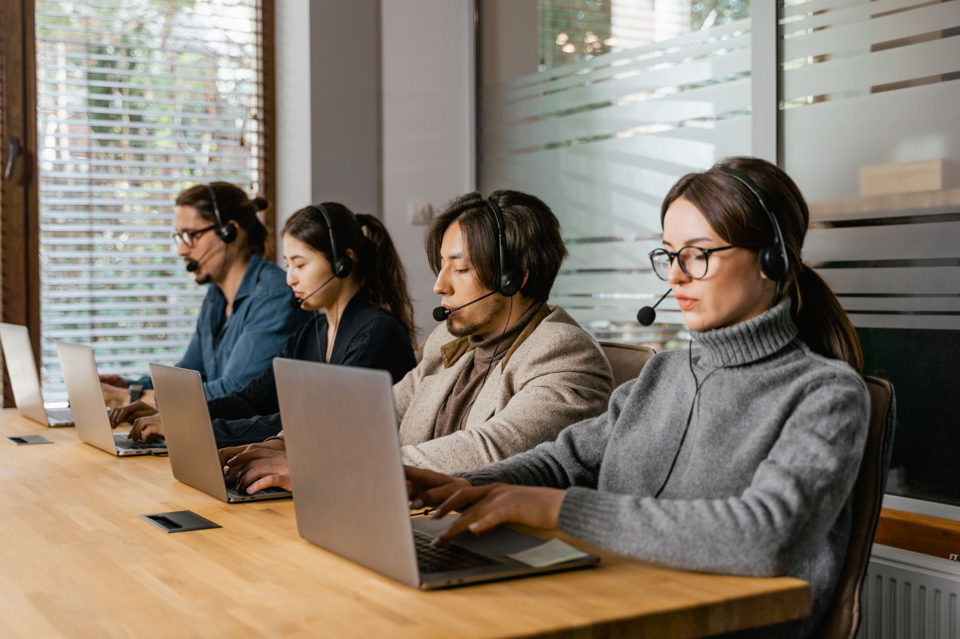 Zespół pracowników call center przy laptopach i w słuchawkach