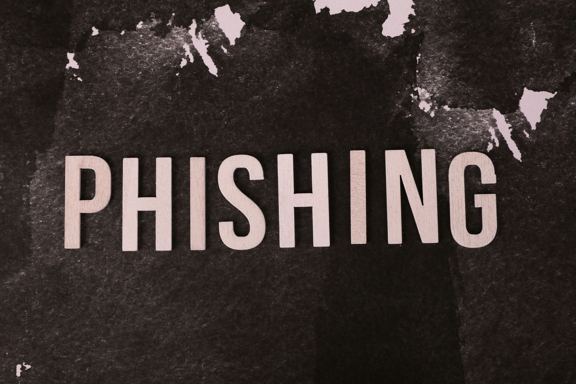 Phishing przez SMS: jak działa smishing i jak go uniknąć Abstrakcyjna grafika z napisem phishing na ciemnym, fakturowanym tle